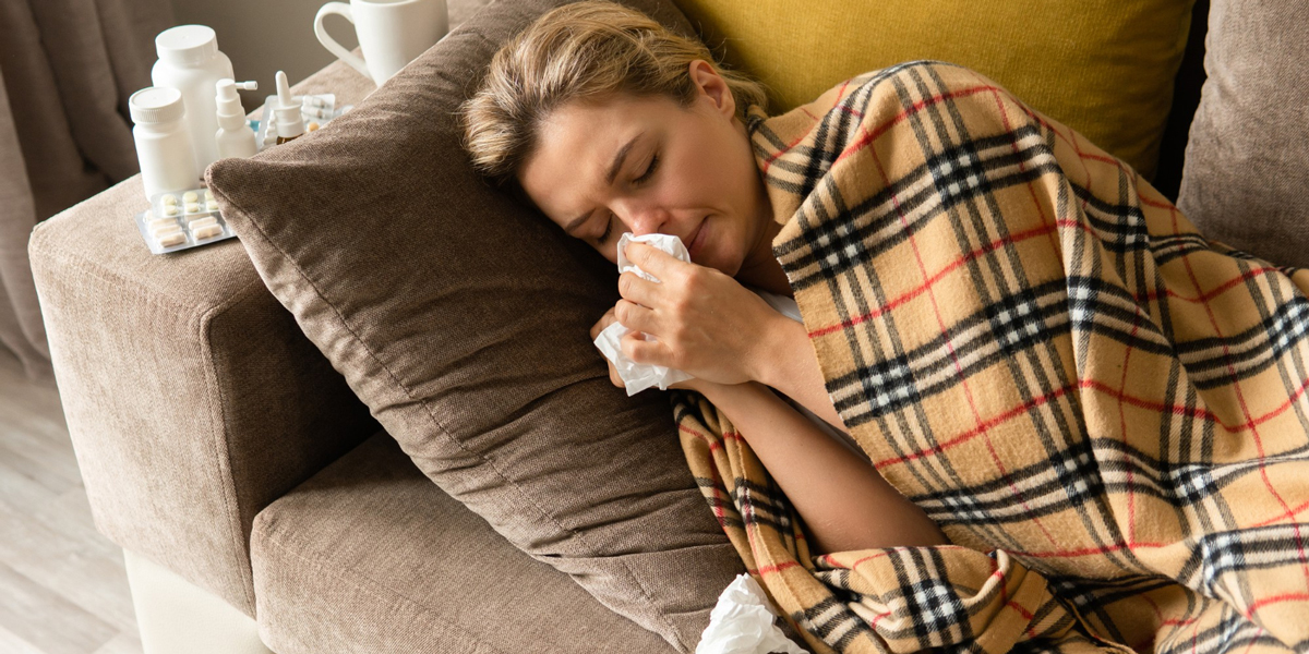 Donna con un sintomo di influenza con naso che cola sdraiata sotto la coperta a casa